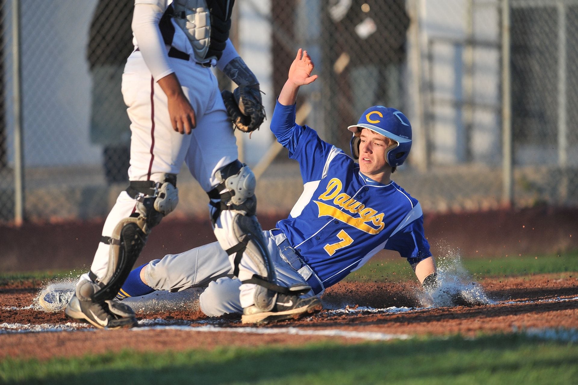 High school baseball player in a custom blue and gold jersey sliding into home plate